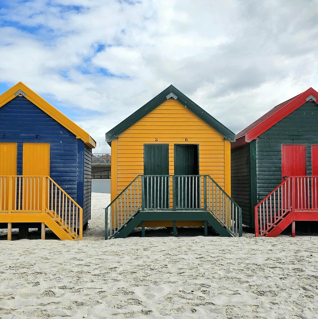 A row of vibrant beach huts on the sandy shore of Muizenberg in Cape Town.