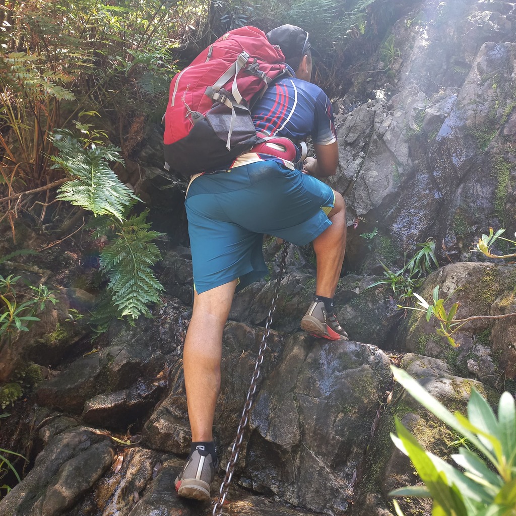 A VDK guide climbing a chain on a mountain hiking trail.