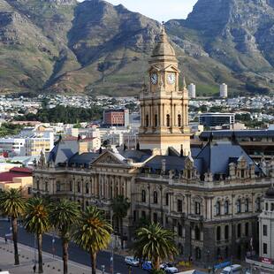 Table Mountain covered in clouds with the city beneath it and red and white flowers in the forefront.